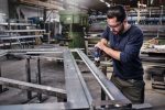Ein Arbeiter mit Sicherheitsausrüstung bohrt Löcher in einen Metallrahmen in einer Fabrik.