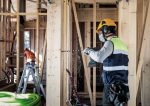 Ein Arbeiter mit Sicherheitsausrüstung bohrt auf einer Baustelle in einen Holzbalken.