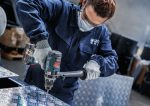 Eine Person mit Sicherheitsausrüstung bohrt ein Loch in gemustertes Metall.