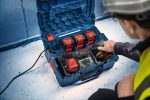 Eine Person mit Sicherheitsausrüstung bedient auf einer Baustelle eine Ladestation für mehrere Batterien.