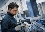 Eine Person, die Schutzausrüstung trägt, bohrt in einen Metallrahmen.
