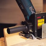 Ein elektrischer Hobel glättet ein Holzbrett auf einer Werkbank.